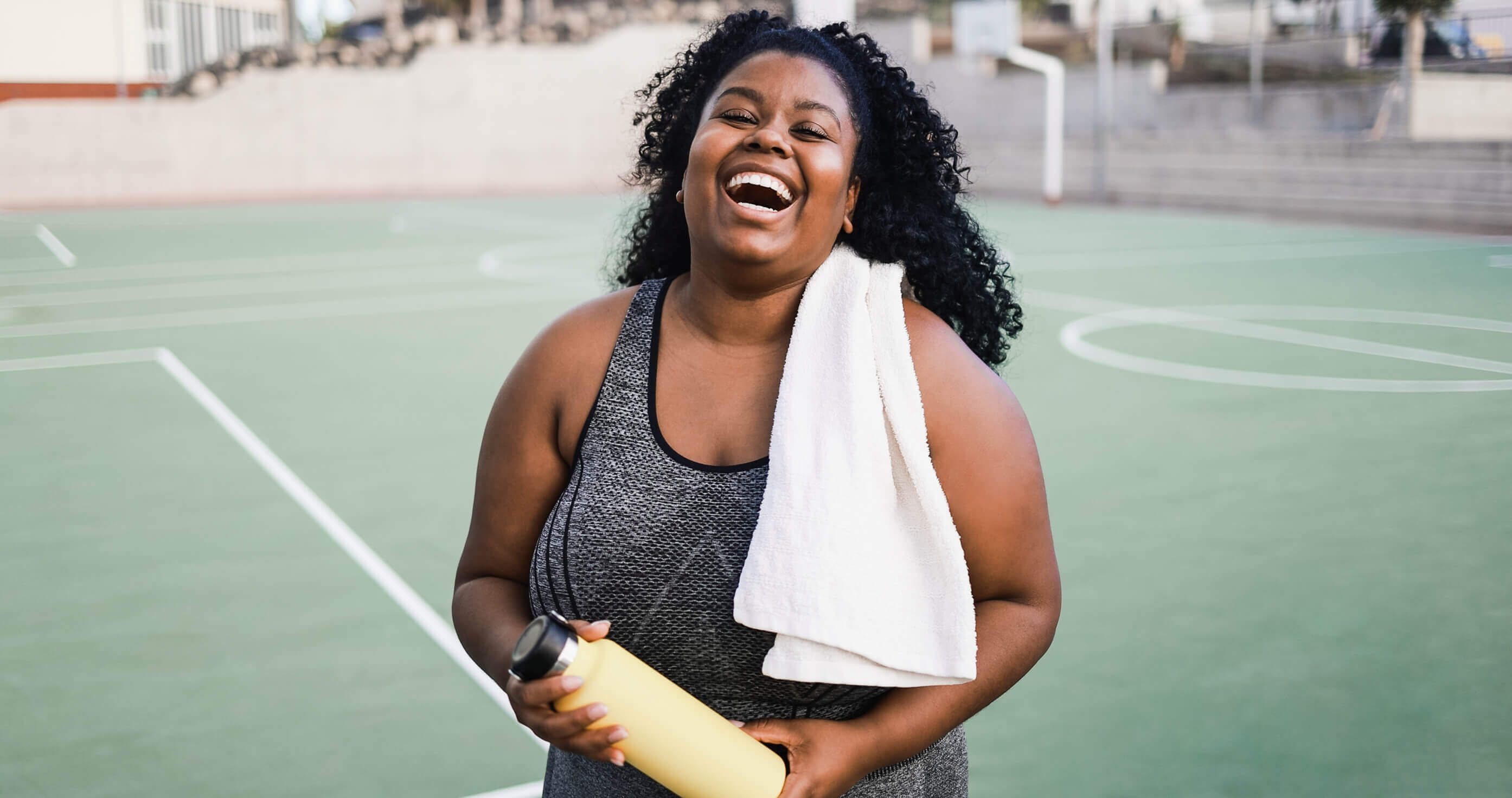 Woman laughing while holding a water bottle after exercise